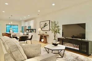 Ein modernes Wohnzimmer mit Sofa, Fernseher, Kamin, Essbereich, Küche und Kunstwerken an der Wand.