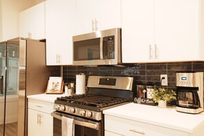 A modern kitchen with stainless steel appliances, a microwave, a coffee maker, and a gas stove. - Downtown Skyline Views | Rooftop Patio | Sleeps 7+ (Des Moines)