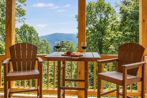 Eine Holzterrasse mit zwei Stühlen und einem Tisch, einem Glas Rotwein und einem Teller Käse und Trauben.