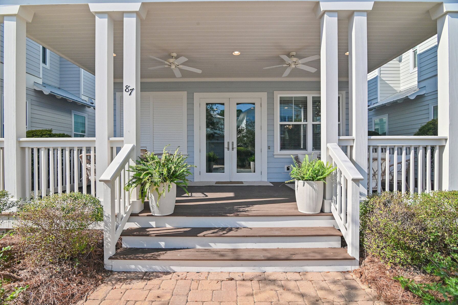 A two-story house with a covered porch, white railings, and a number '87' on the wall.