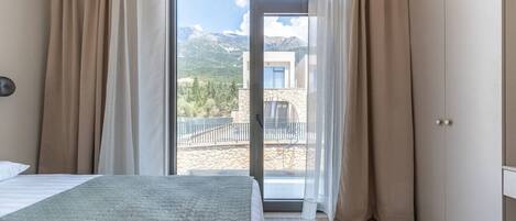 A bedroom with a bed, a sliding glass door to a balcony, and a view of mountains.