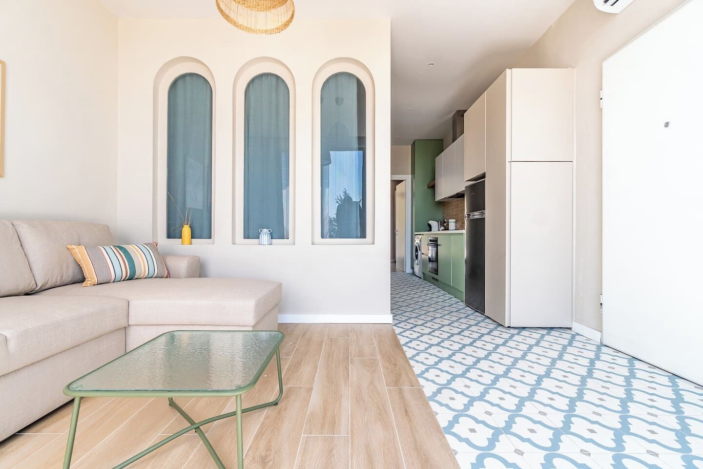 A modern living room with a sofa, a glass coffee table, and a kitchen with a patterned floor.