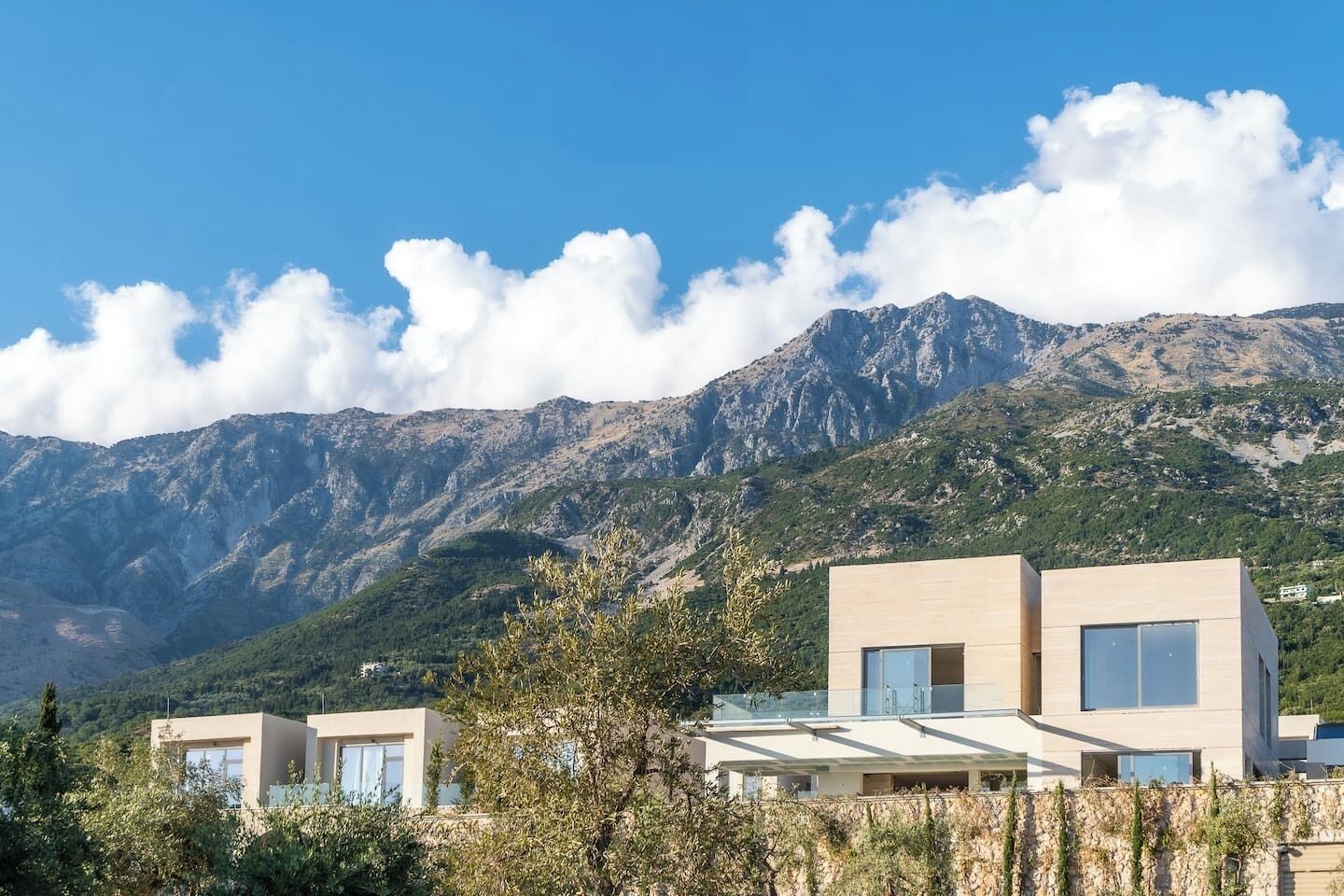 A modern building with a flat roof and large windows, surrounded by lush greenery and mountains in the background.