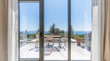 A view through a sliding glass door to an outdoor patio with a table and chairs, overlooking a coastal landscape.