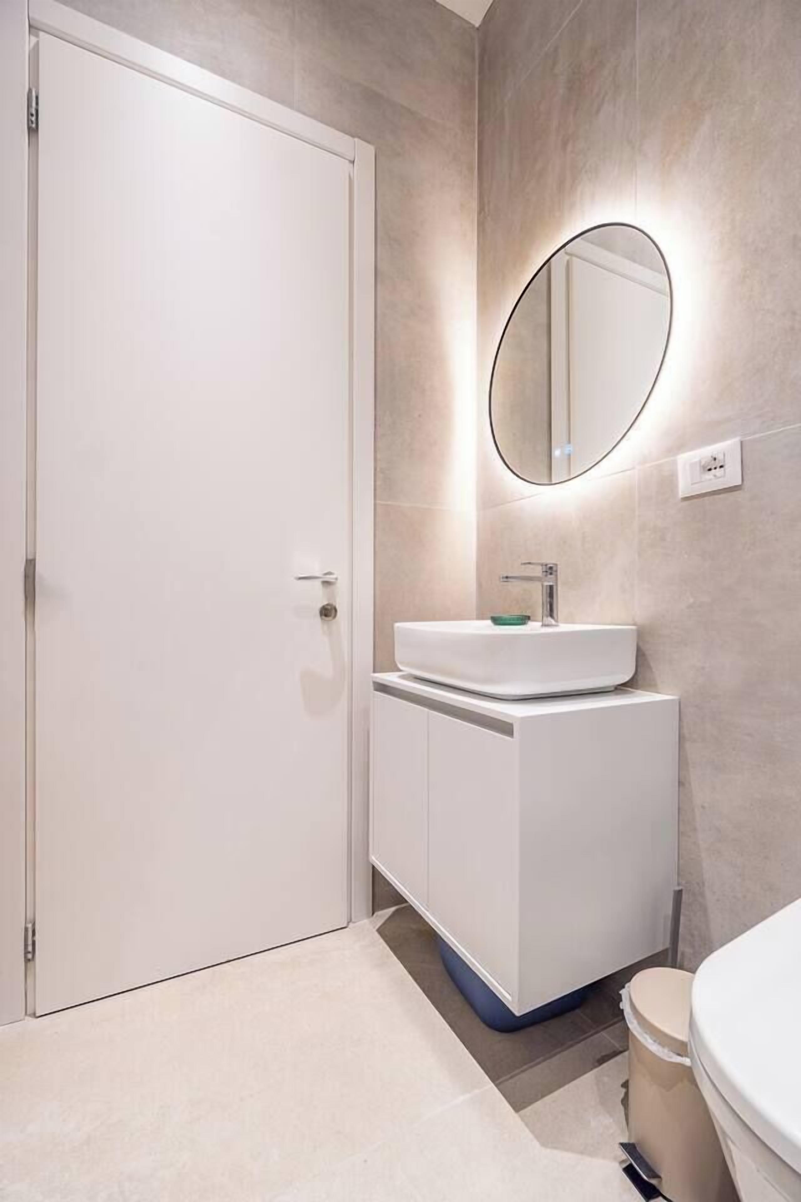 A bathroom with a white vanity, a round mirror, and a toilet.