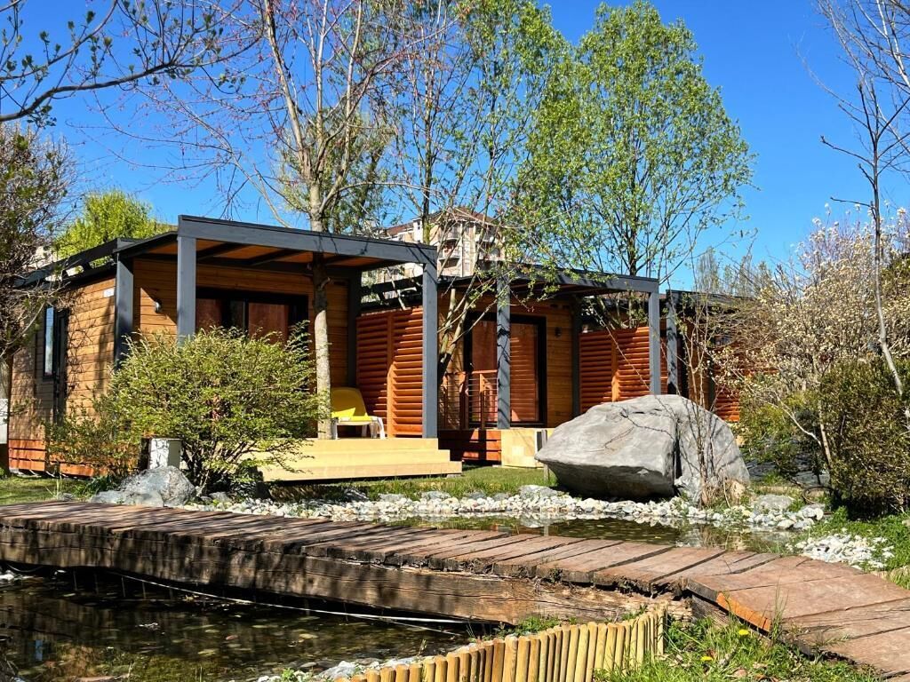 Een modern blokhut met een overdekte veranda, een klein vijvertje en een houten bruggetje.