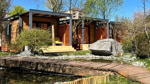Eine moderne Blockhütte mit einer überdachten Veranda, einem kleinen Teich und einer Holzbrücke.