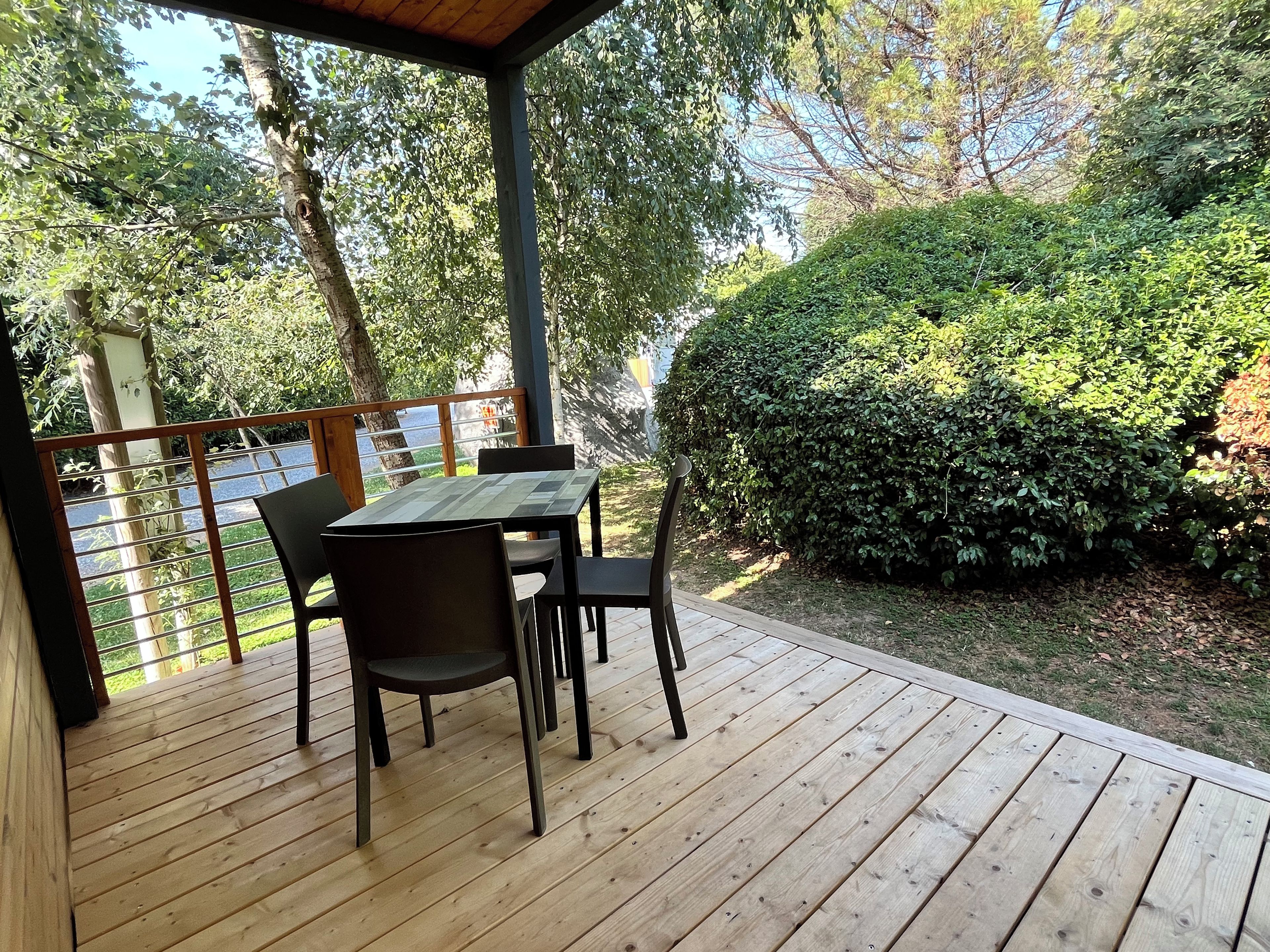 Un espacio de estar al aire libre cubierto, con una mesa y sillas, rodeado de vegetación y vistas a un cuerpo de agua.