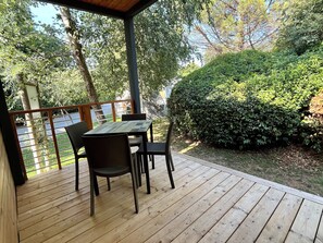 A covered outdoor seating area with a table and chairs, surrounded by greenery and a view of a body of water.