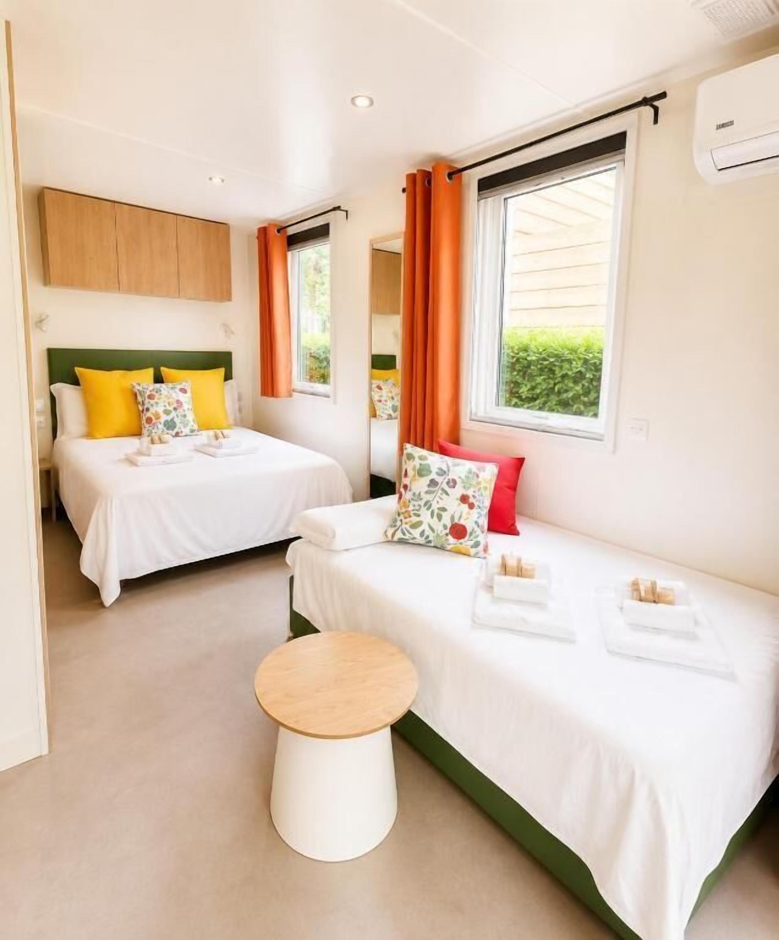 Een hotelkamer met twee bedden, een klein rond tafeltje en een raam met gordijnen.
