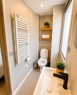 A bathroom with a white bathtub, a toilet, a towel rack, and a small potted plant. - Grinto Urban Eco Village (Moncalieri)