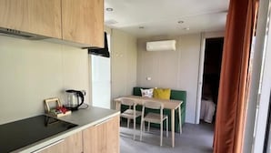 A compact kitchen with a dining area, a window with curtains, and a visible door leading to another room.