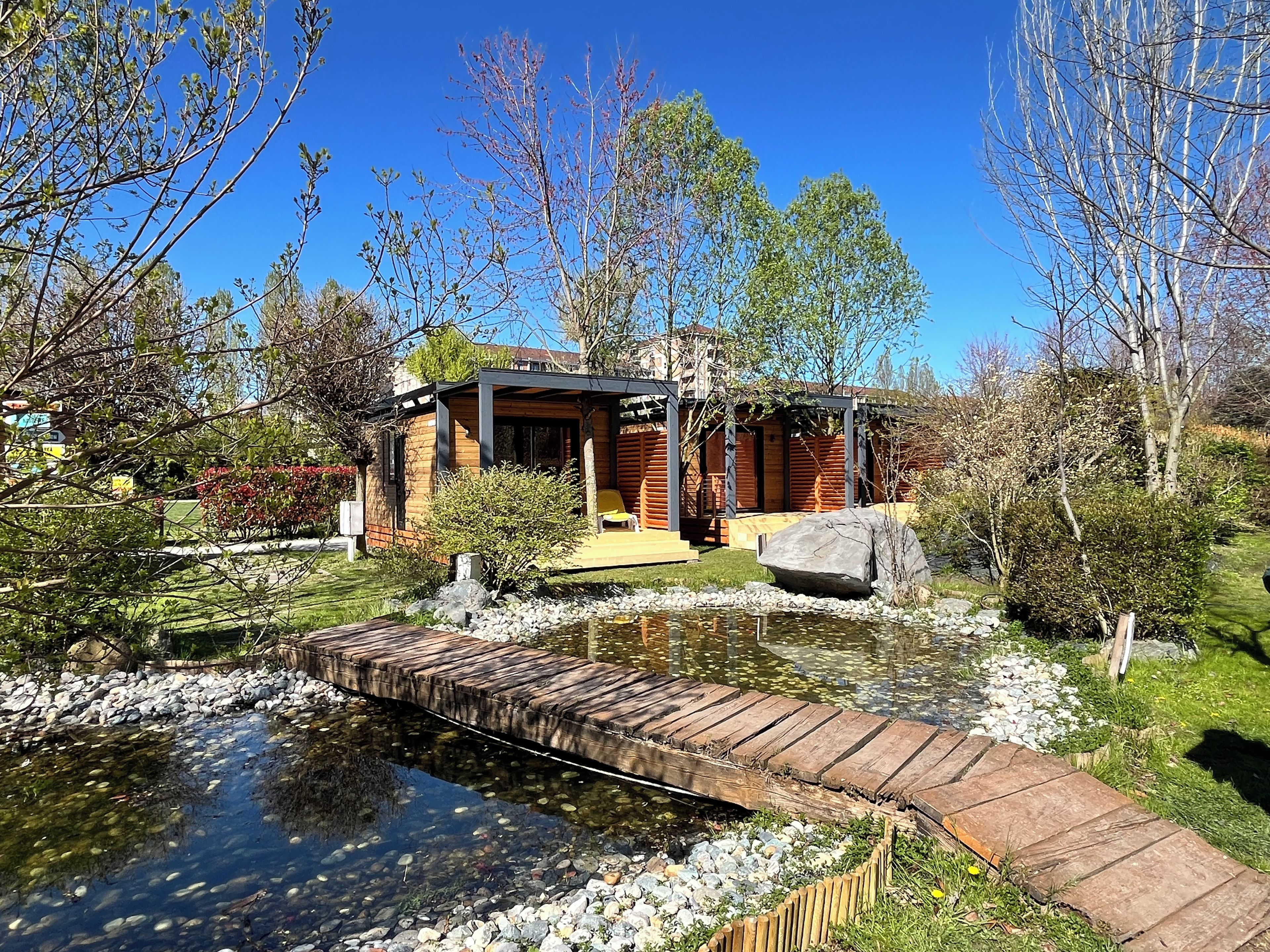 Una casa moderna con terraza de madera, un estanque y un jardín.