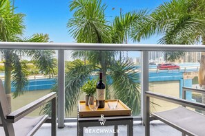 Ein Balkon mit Blick auf Palmen und eine Stadtlandschaft, eine Weinflasche und ein Tablett mit einem Glas.