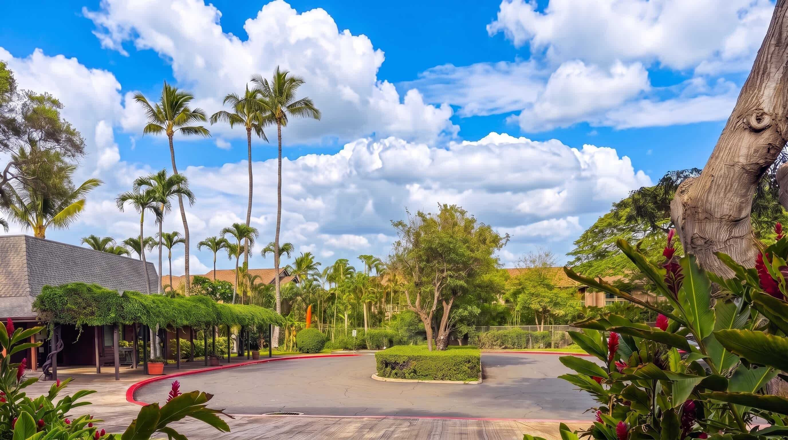 A landscaped area with palm trees, a curved pathway, and a building with a tiled roof.