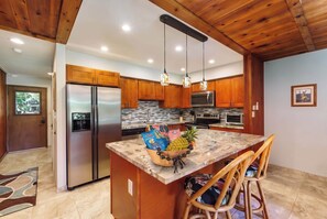 A modern kitchen with wooden cabinets, stainless steel appliances, a granite countertop, and a center island with chairs. - Koa Resort 3E | Two Bedroom Condo in Kihei (Kihei)