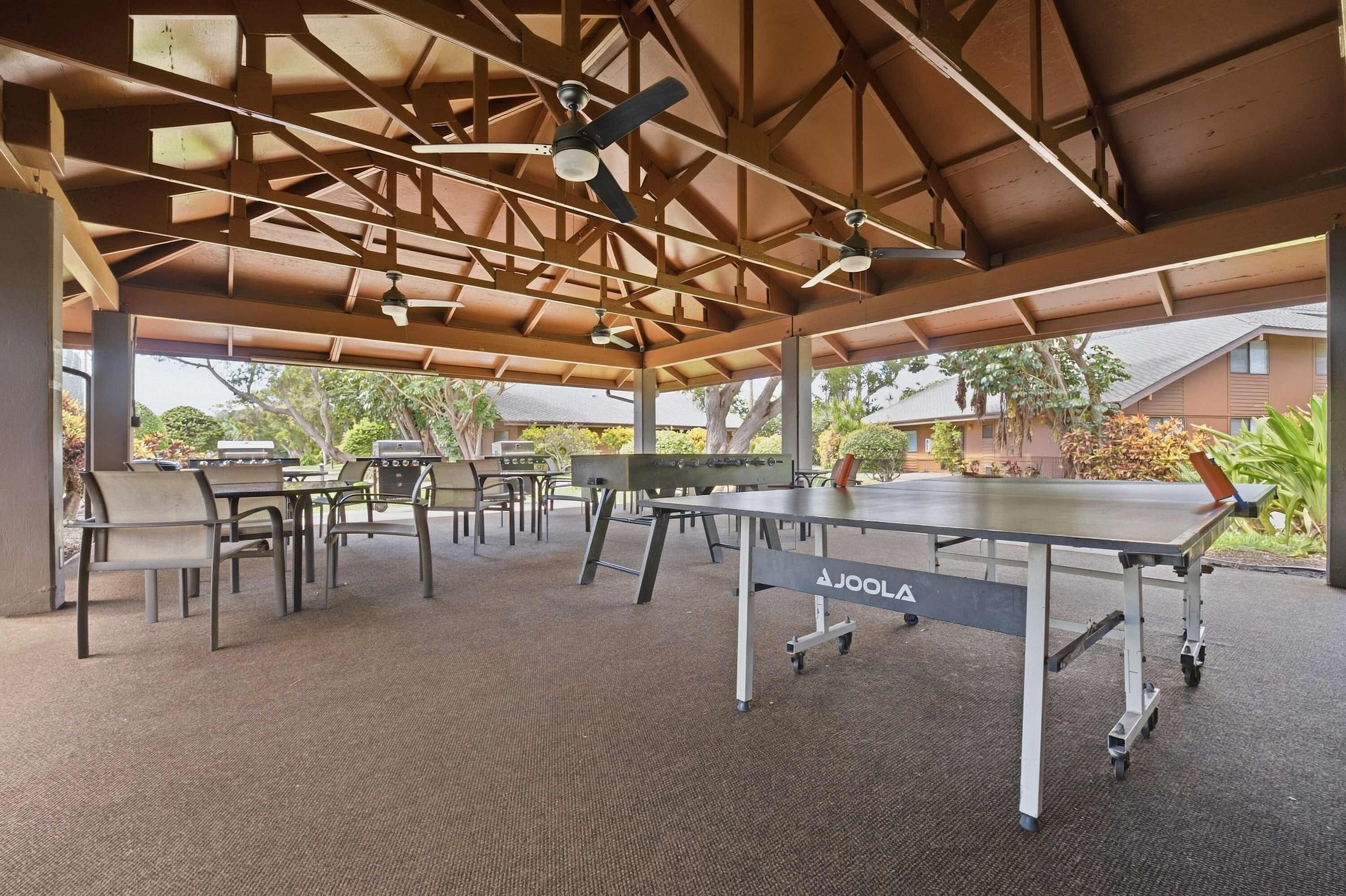 Un espacio al aire libre cubierto con mesas, sillas, una mesa de ping pong y ventiladores de techo.