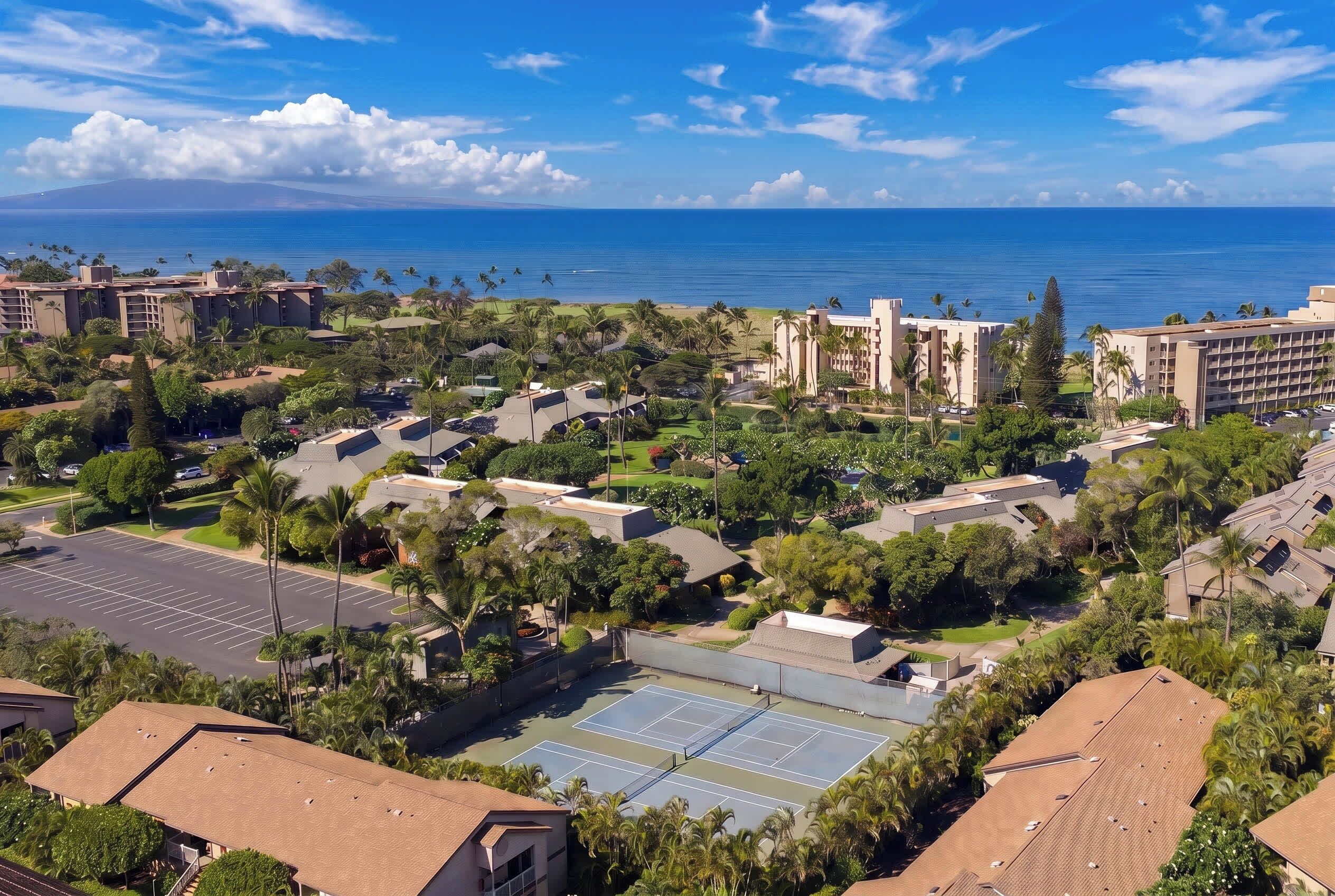 A coastal resort with multiple buildings, a tennis court, and a view of the ocean.