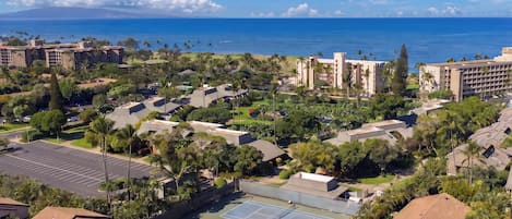 A coastal resort with multiple buildings, a tennis court, and a view of the ocean.