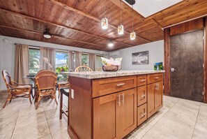 Una cocina con armarios de madera, encimera de mármol y comedor con sillas de mimbre.