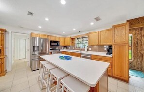 A modern kitchen with wooden cabinets, stainless steel appliances, and a central island with stools. - Peaceful 2/2 in Homosassa Springs Hot Spot (Homosassa Springs)