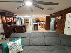 A living room with a grey sofa, a ceiling fan, and a kitchen in the background. - Peaceful 2/2 in Homosassa Springs Hot Spot (Homosassa Springs)