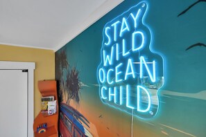 A wall with a neon sign that reads 'STAY WILD OCEAN CHILD.' - 27 Steps to Beach and BOOM you’re there + Secret Game Room + Rooftop Deck (Carolina Beach)