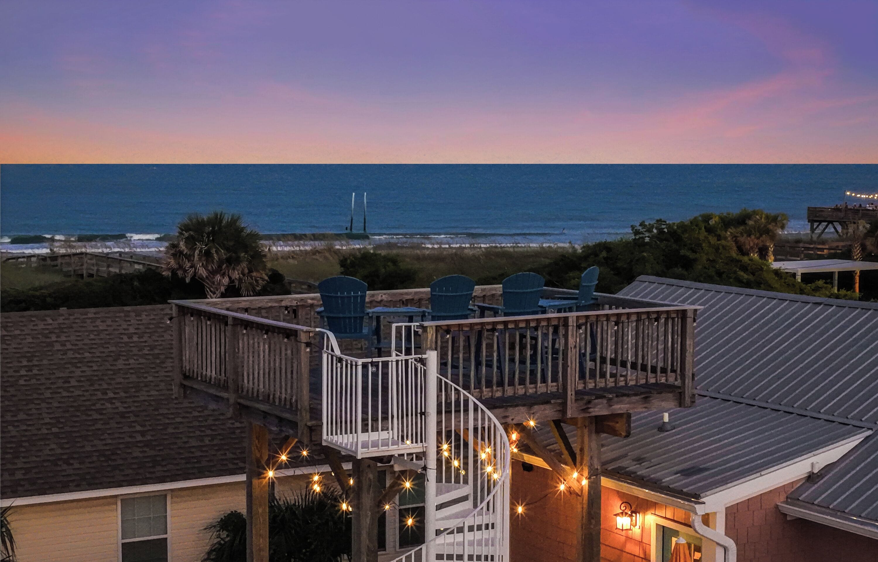 A deck with outdoor seating overlooking a beach and ocean.
