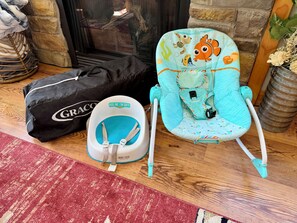 Un transat pour bébé avec un jouet en peluche, un sac noir orné du logo « GRACO » et un coussin bleu posé sur un plancher en bois.