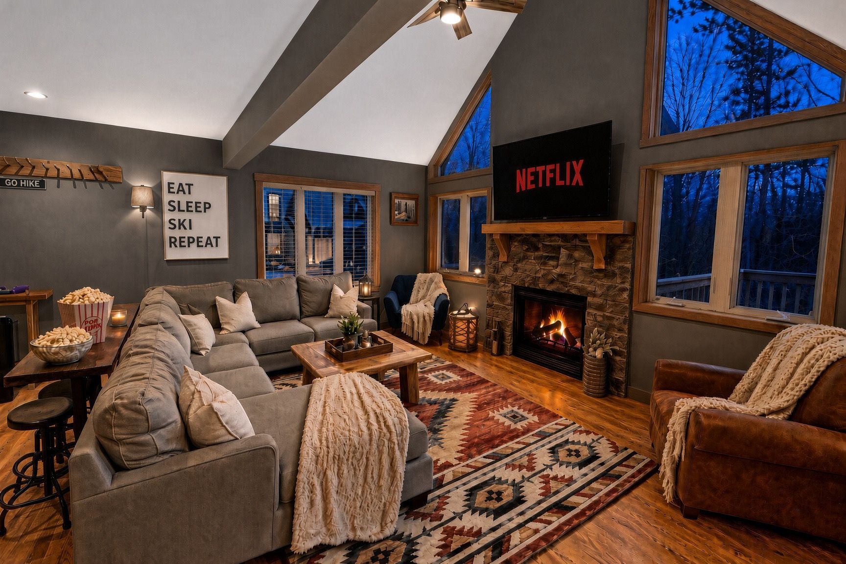 Ein gemütliches Wohnzimmer mit Kamin, einem Netflix-Schild und einem großen Fenster mit Blick auf Bäume.