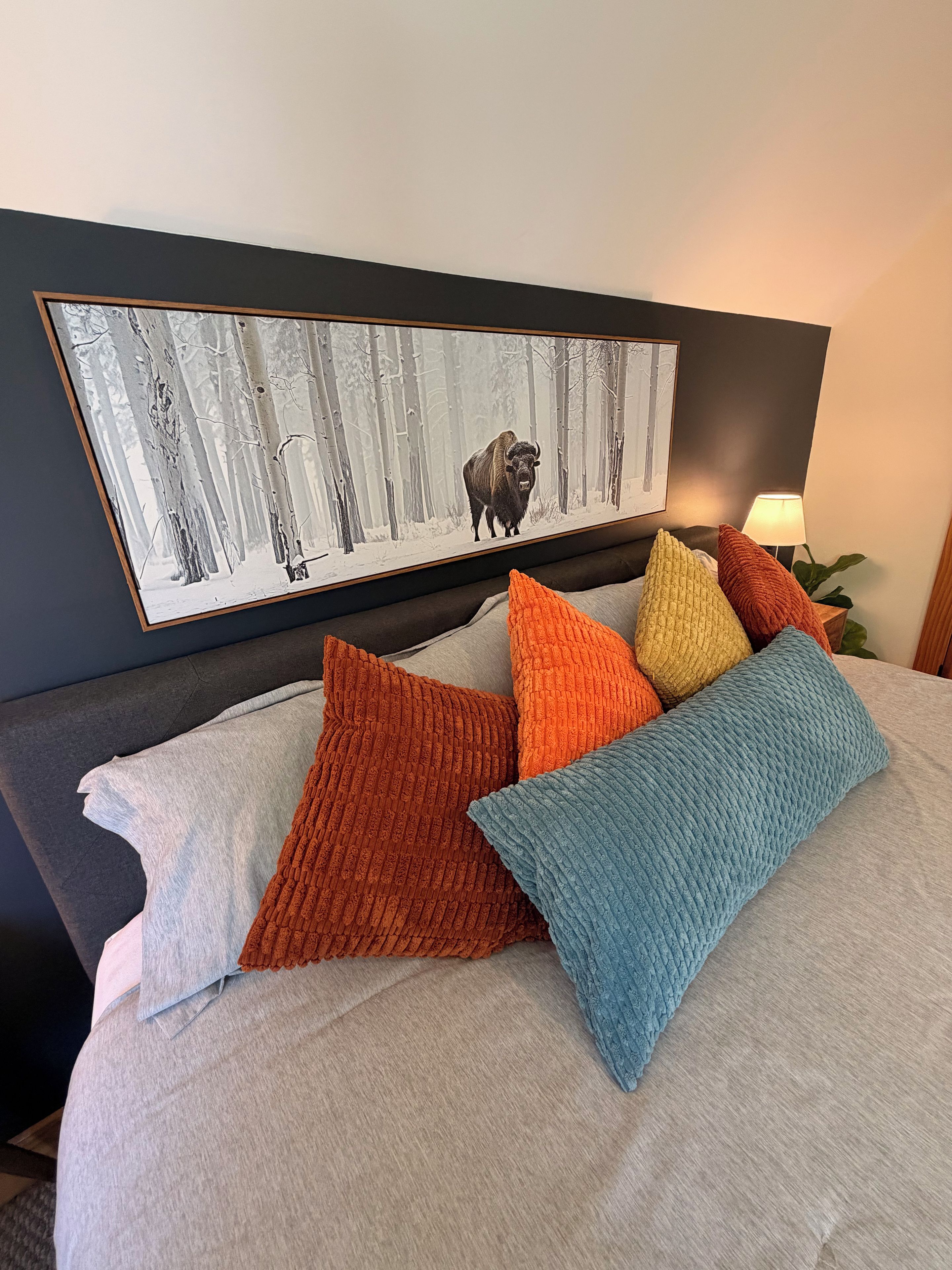 A bed with a gray bedspread and multiple colorful pillows.