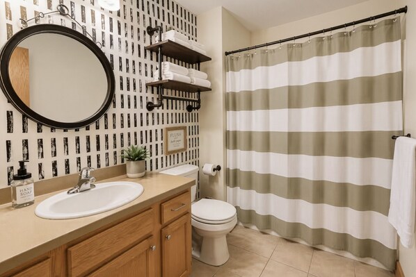 A bathroom with a round mirror, a sink, a toilet, a shower curtain, and a towel rack.
