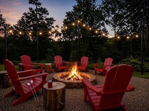 A fire pit surrounded by red Adirondack chairs, with string lights overhead.