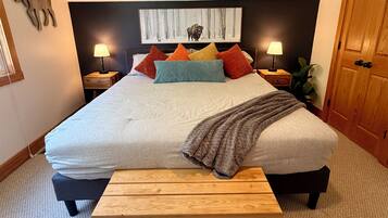 A bedroom with a large bed, multiple pillows, bedside lamps, a wooden bench, and a moose decoration on the wall.