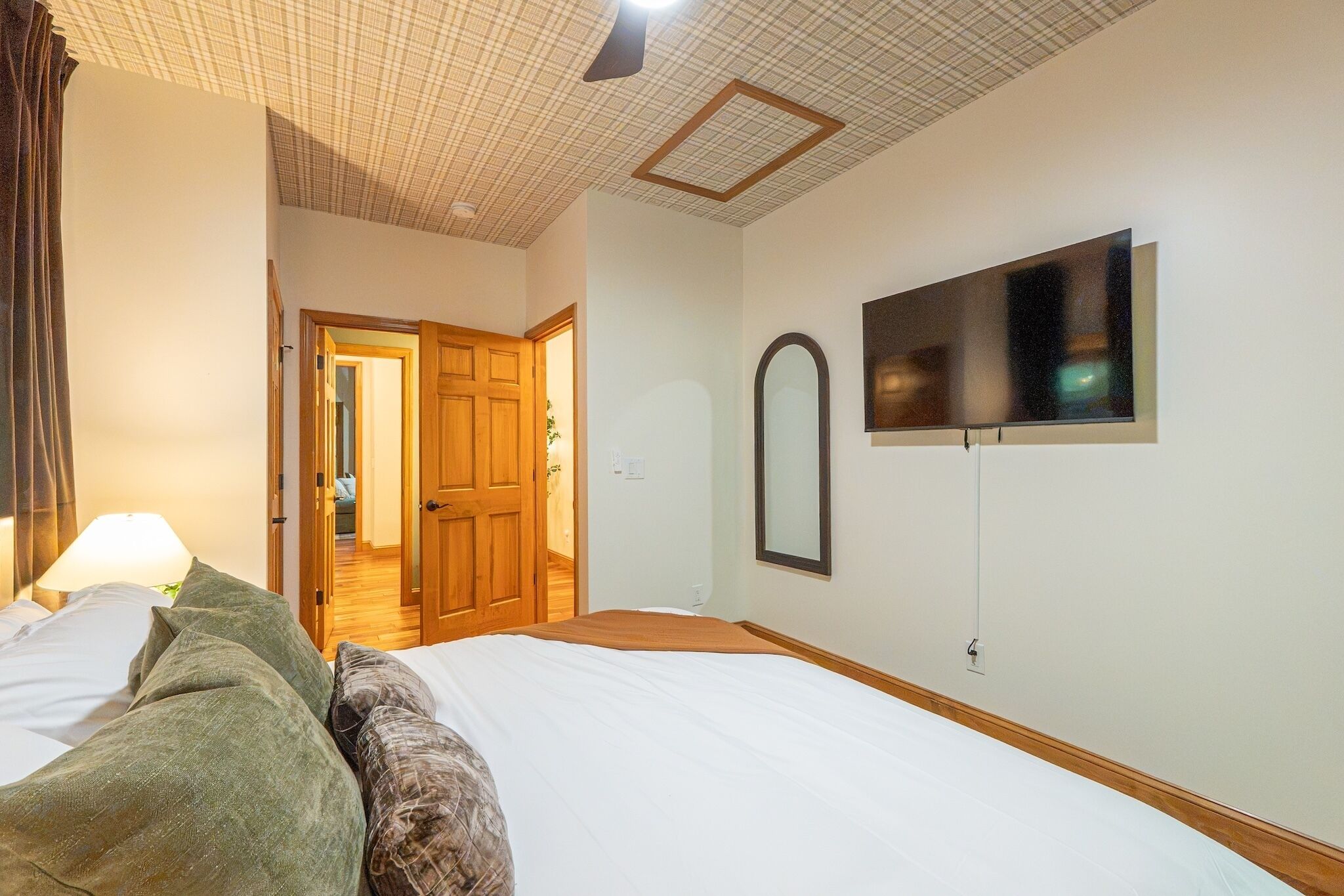 Ein Hotelzimmer mit Bett, Wandfernseher, einer Tür zu einem anderen Raum und Deckenventilator.