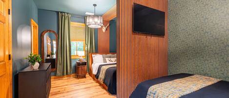 Een moderne hotelkamer met een houten vloer, een bed met een bed met een patroon, een bureau met een plant, een spiegel en een televisie aan de muur.