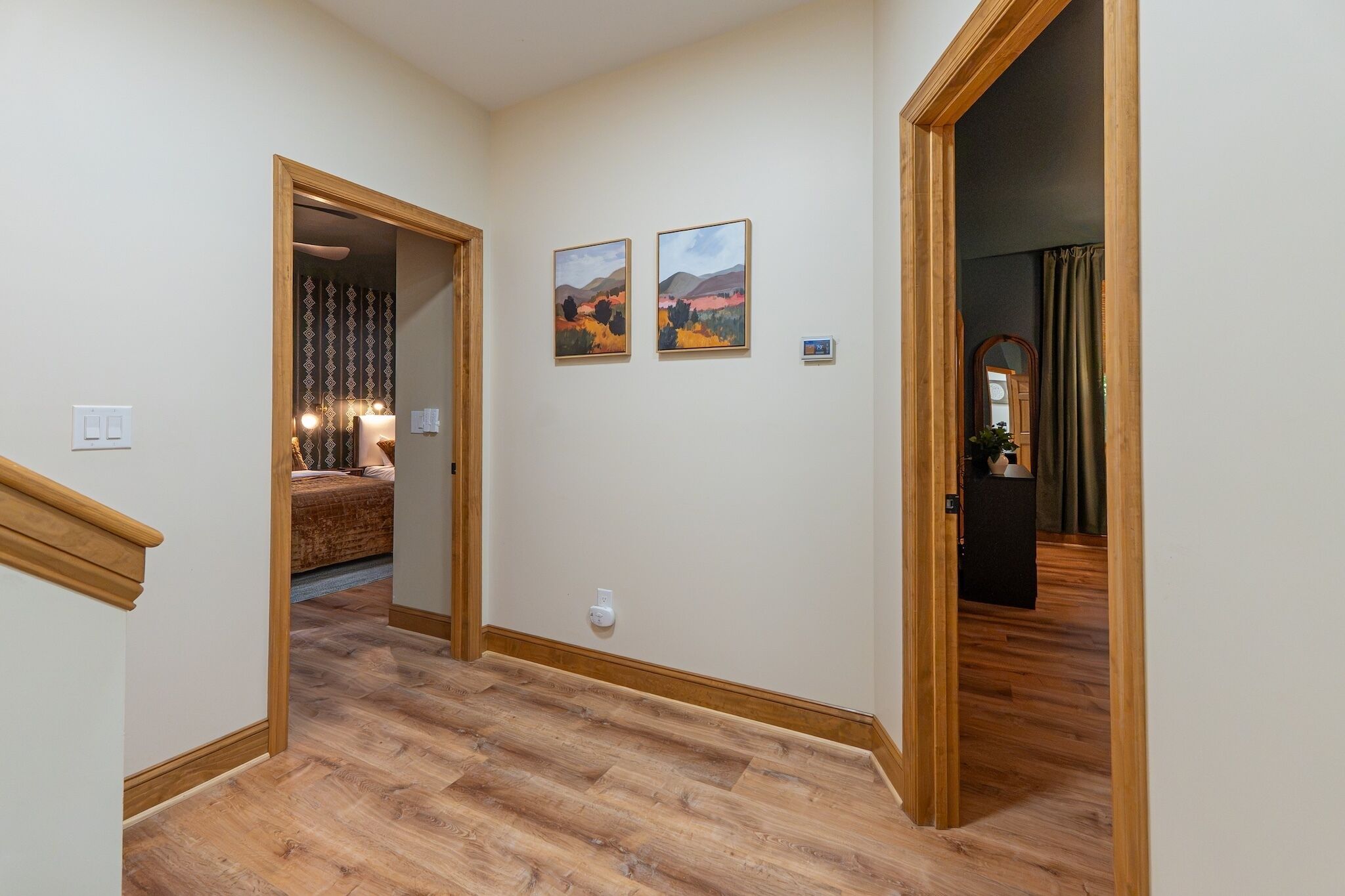 A hallway with wooden flooring, a bed with patterned bedding, and two landscape paintings on the wall.
