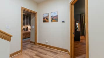 A hallway with wooden flooring, a bed with patterned bedding, and two landscape paintings on the wall.