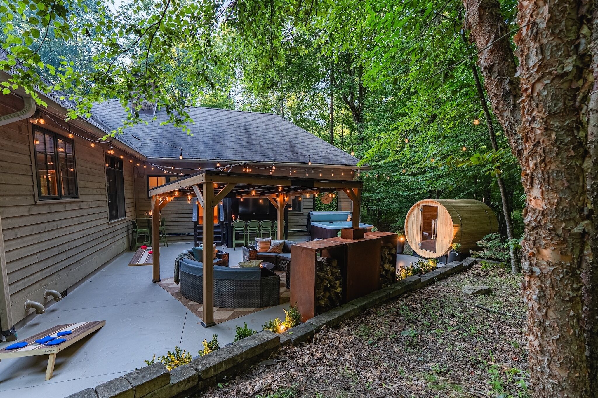 A covered outdoor seating area with a hot tub, wooden deck, and string lights.