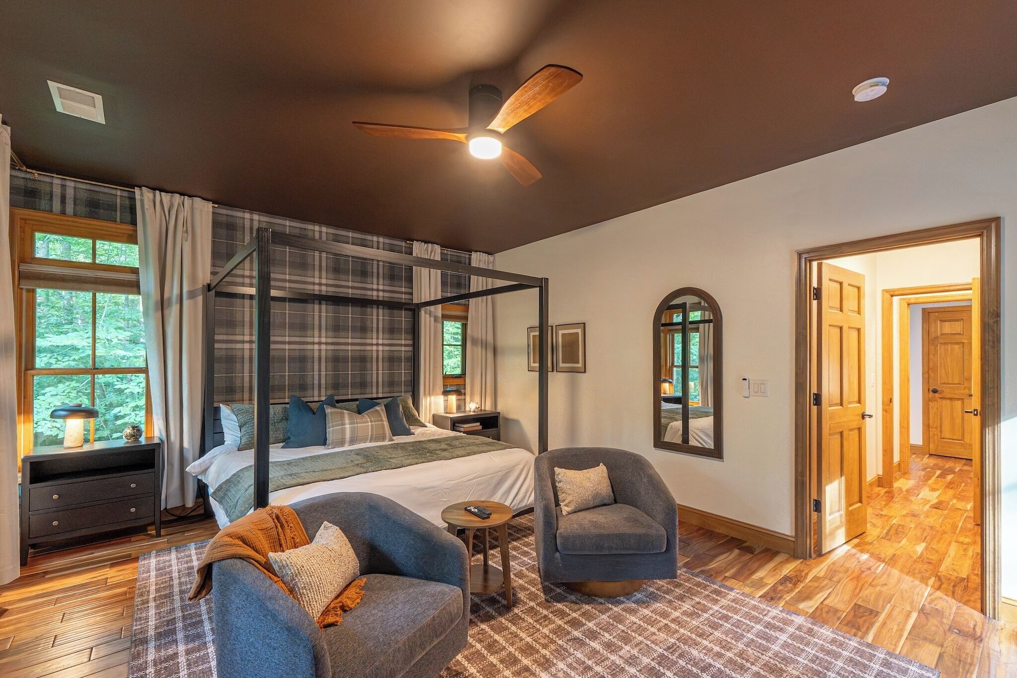 A bedroom with a four-poster bed, a ceiling fan, and a view of the outdoors through a window.