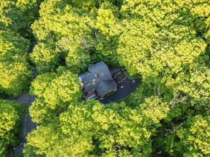 Une vue aérienne d’une propriété entourée d’une végétation luxuriante, avec une allée pavée menant à un bâtiment doté d’un toit en pente.