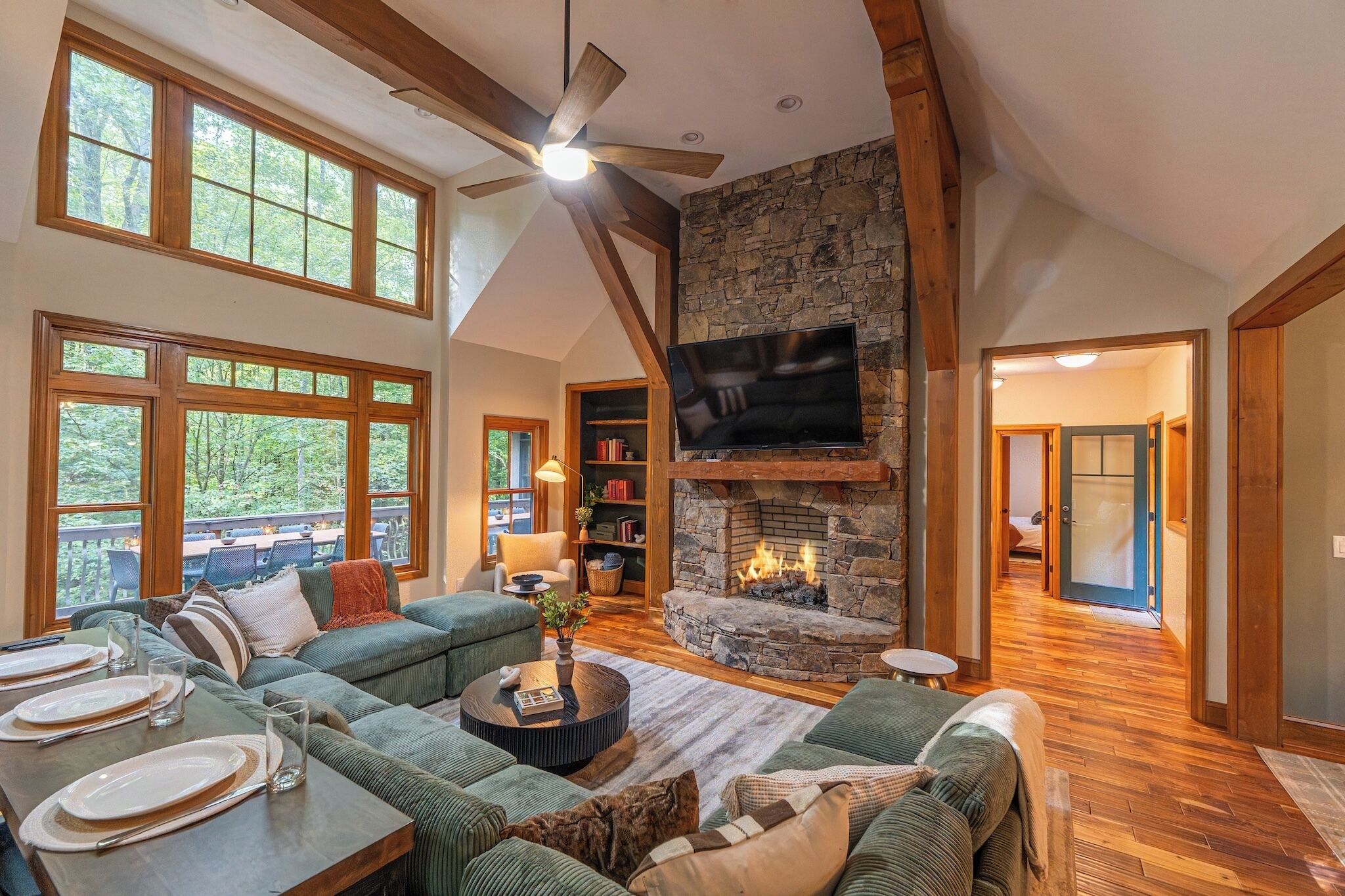 A spacious living room with a stone fireplace, a ceiling fan, and a large TV mounted on the wall.