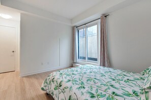 Une chambre à coucher avec un lit, une fenêtre avec des rideaux, une porte et un interrupteur sur le mur.