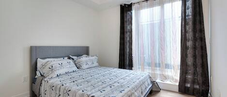 Un dormitorio con cama, ventana con cortinas y un interruptor de luz en la pared.