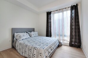 Ein Schlafzimmer mit Bett, einem Fenster mit Vorhängen und einem Lichtschalter an der Wand.
