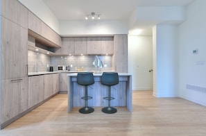 Una cocina moderna con armarios de madera, una isla central con dos taburetes de bar y un microondas.