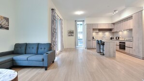En moderne stue med en grå sofa, et spiseområde med barstole og et køkken med træskabe og en central ø.