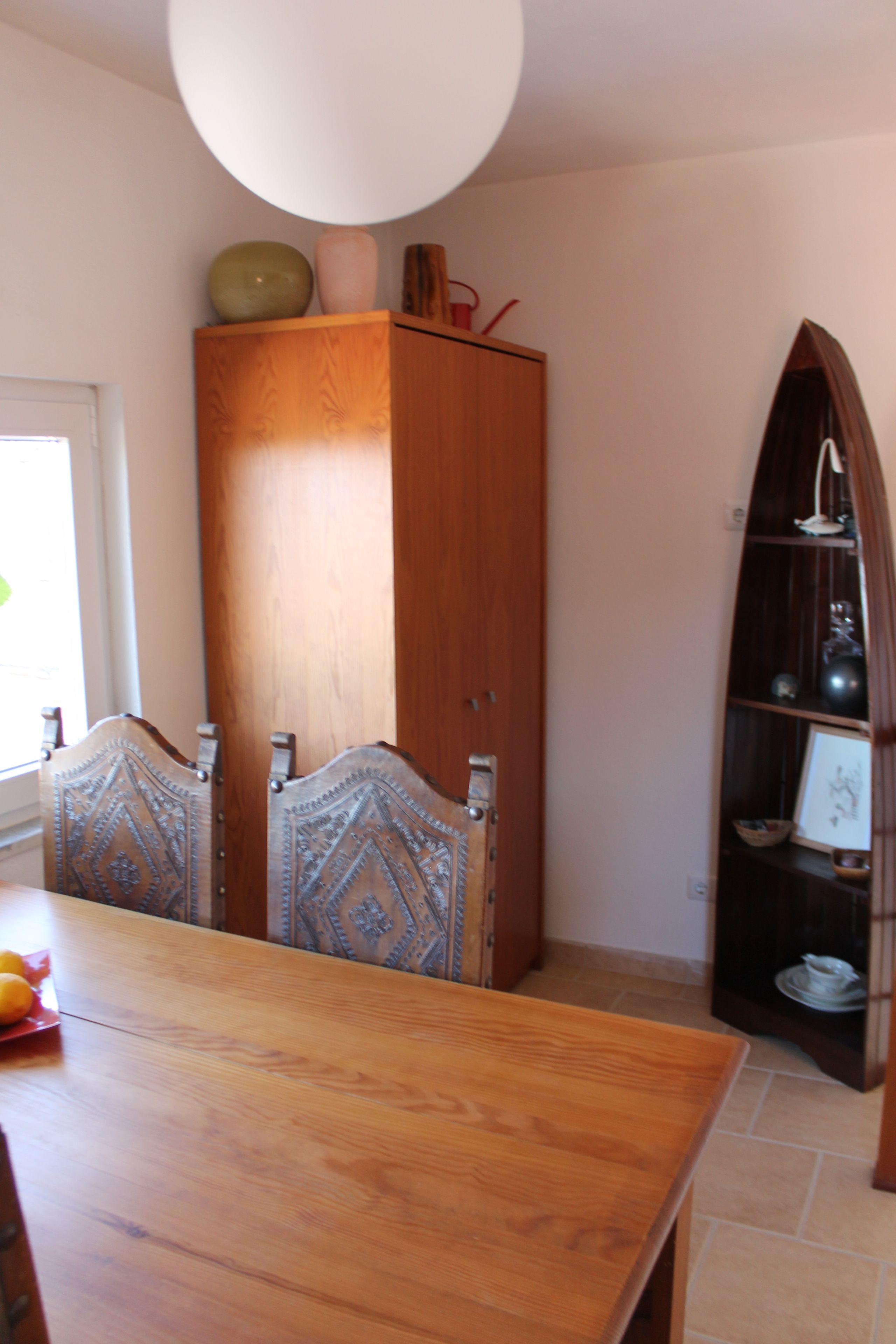 Een eethoek met een houten tafel en stoelen, een kast en een plank met decoratieve objecten.