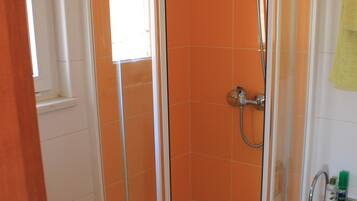 Un baño en esquina con ducha envuelta en vidrio, un lavabo blanco y un inodoro.