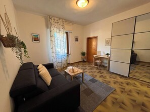 Ein Wohnzimmer mit einer schwarzen Couch, einem kleinen Holztisch und einem gemusterten Teppich.
